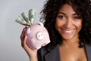Labor Law Legal Funding | Only Pay Us Back If You Win | Free Application A woman of color holds a piggy bank with three twenty-dollar bills sticking out of it and smiles.