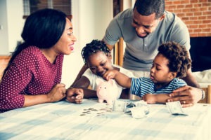 family counts money with piggy bank at kitchen table
