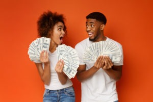 excited young couple holding wads of cash