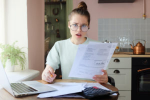 A young woman in her kitchen, looking shocked about her bills.